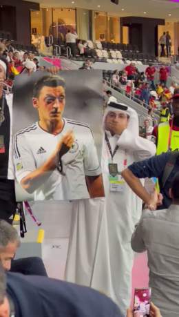 A fan goes around the Germany fans holding up a poster of Mesut Ozil and covering his mouth.